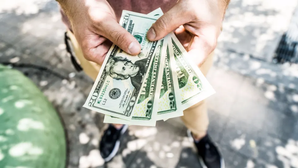 One person handing a fan of dollar bills to another.